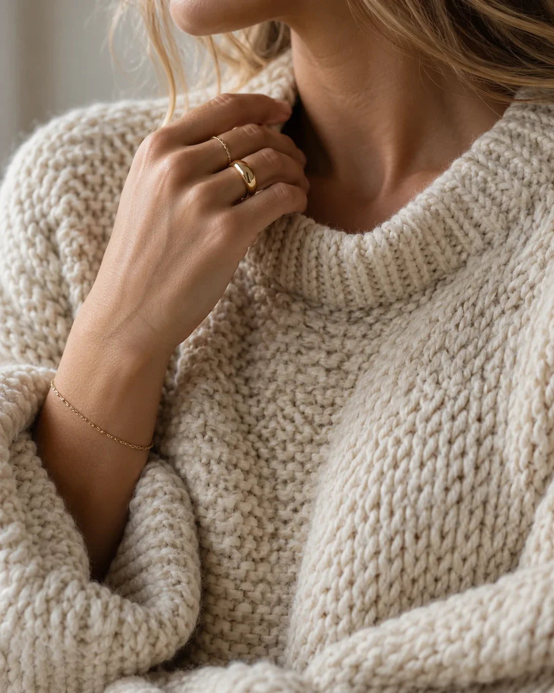 Detalle de tejido de punto crema con joyeria dorada