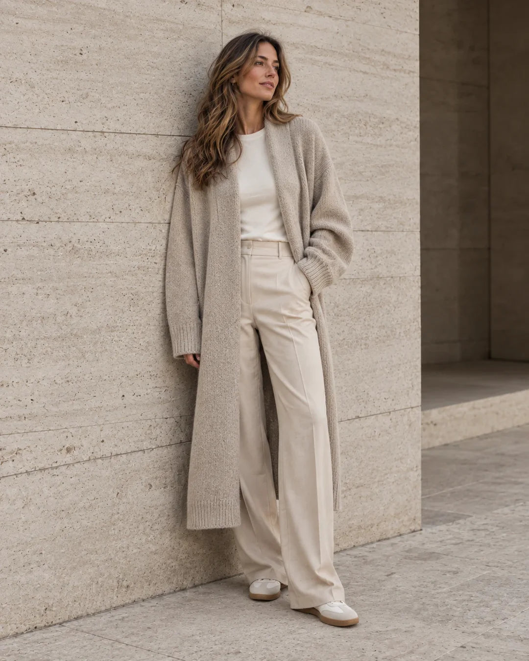 Mujer con cardigan de punto largo contra pared de piedra, estilo de vida